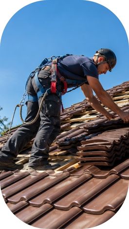 Couvreur professionnel posant des tuiles neuves sur la toiture d’une maison en rénovation.